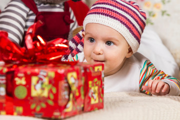 Fototapeta na wymiar close-up of a smiling baby in a knitted hat lying on his stomach on the sofa among gifts and toys on New Year's theme