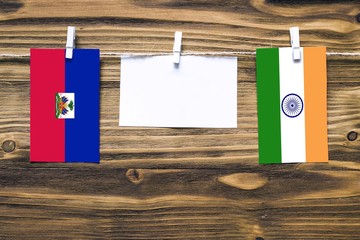 Hanging flags of Haiti and India attached to rope with clothes pins with copy space on white note paper on wooden background.Diplomatic relations between countries.