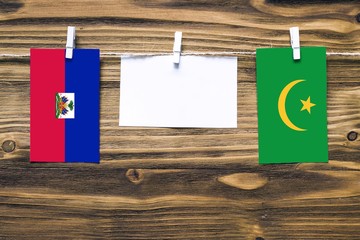 Hanging flags of Haiti and Mauritania attached to rope with clothes pins with copy space on white note paper on wooden background.Diplomatic relations between countries.