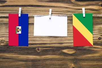 Hanging flags of Haiti and Republic Of The Congo attached to rope with clothes pins with copy space on white note paper on wooden background.Diplomatic relations between countries.