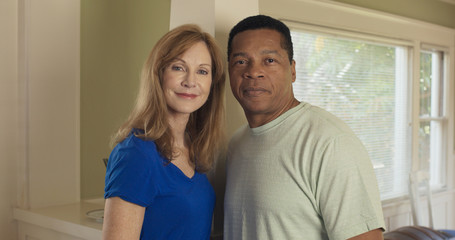 Mature Caucasian and African American couple standing in their home smiling