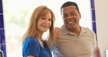 older Caucasian and African American couple standing in their kitchen smiling