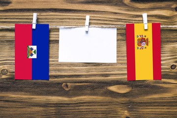 Hanging flags of Haiti and Spain attached to rope with clothes pins with copy space on white note...