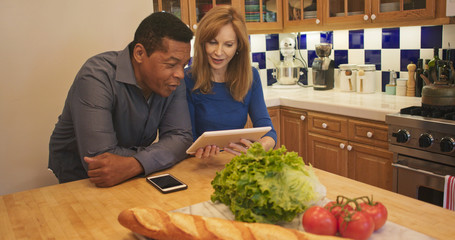 Senior couple standing in kitchen looking at recipe on tablet computer