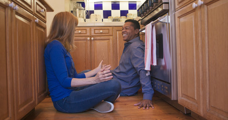 couple sit on floor of kitchen talking while waiting for oven to finish baking