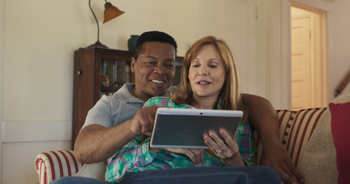 Older Couple On The Couch Using Tablet Computer Together To Watch Funny Video