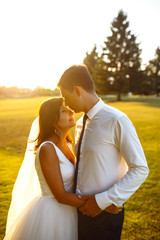 Lovely wedding couple at sunset. Bride and groom in wedding attire with a bouquet of flowers is in the hands against the backdrop of the  green field at sunset. Romantic Married young family. 