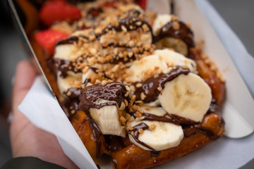 Hand holding homemade Belgian waffles with honey, banana, strawberry and chocolate background