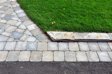 This landscape project shows a professionally designed and crafted transition from walkway to driveway, and uses natural stone curbing to minimize the grade between lawn and pavers. - obrazy, fototapety, plakaty