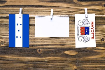 Hanging flags of Honduras and Mayotte attached to rope with clothes pins with copy space on white note paper on wooden background.Diplomatic relations between countries.