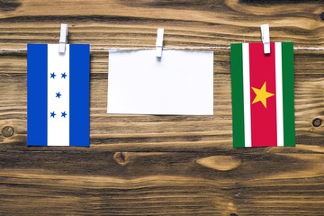 Hanging flags of Honduras and Suriname attached to rope with clothes pins with copy space on white note paper on wooden background.Diplomatic relations between countries.