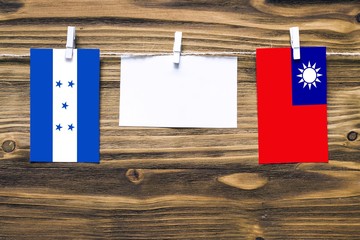 Hanging flags of Honduras and Taiwan attached to rope with clothes pins with copy space on white note paper on wooden background.Diplomatic relations between countries.