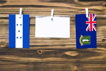 Hanging flags of Honduras and British Virgin Islands attached to rope with clothes pins with copy space on white note paper on wooden background.Diplomatic relations between countries.