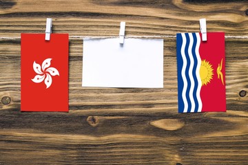Fototapeta premium Hanging flags of Hong Kong and Kiribati attached to rope with clothes pins with copy space on white note paper on wooden background.Diplomatic relations between countries.