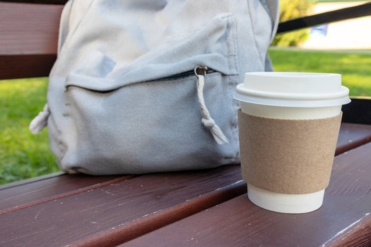 A Craft Disposable Paper Cup Of Coffee And A Backpack On A Bench In Park, Coffee Brake On The Open Air