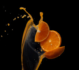 Orange juice with orange fruit slices splash or explosion flying in the air isolated on black background