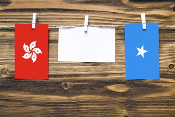 Hanging flags of Hong Kong and Somalia attached to rope with clothes pins with copy space on white note paper on wooden background.Diplomatic relations between countries.