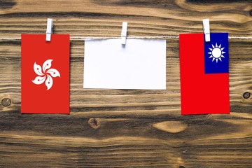 Hanging flags of Hong Kong and Taiwan attached to rope with clothes pins with copy space on white note paper on wooden background.Diplomatic relations between countries.