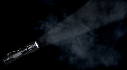 Flashlight with a light beam on dark smoke background