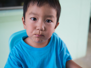Asian child boy in blue t shirt eating and chewing food in mouth at home with happy face on blue chair,food time,healthy concept.