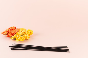 Black incense sticks with orange and yellow flowers on pink background