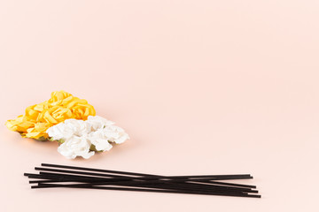 Black incense sticks with white and yellow flowers on pink background