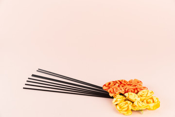 Incense sticks with orange and yellow flowers on pink background