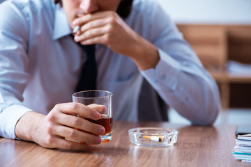 Male employee drinking alcohol and smoking cigarettes at workpla