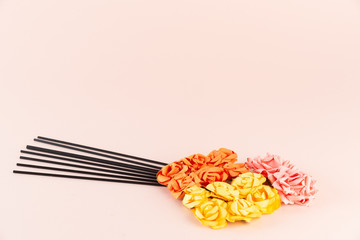 Incense sticks with pink, orange and yellow flowers on pink background