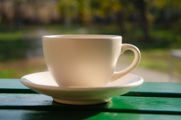 Obraz premium White cup with coffee in the garden on a wooden table.