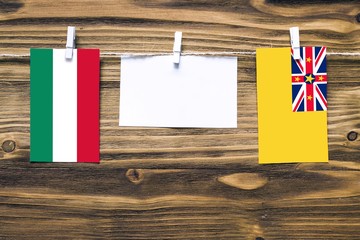 Hanging flags of Hungary and Niue attached to rope with clothes pins with copy space on white note paper on wooden background.Diplomatic relations between countries.