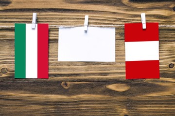 Hanging flags of Hungary and Peru attached to rope with clothes pins with copy space on white note paper on wooden background.Diplomatic relations between countries.