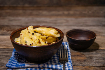 Dumplings with potatoes and onion frying in a ceramic bowl, napkin, fork and pottery with sour cream.