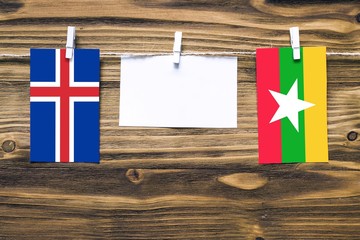 Hanging flags of Iceland and Myanmar attached to rope with clothes pins with copy space on white note paper on wooden background.Diplomatic relations between countries.