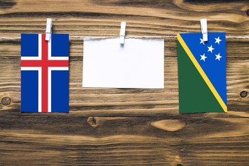 Hanging flags of Iceland and Solomon Islands attached to rope with clothes pins with copy space on...