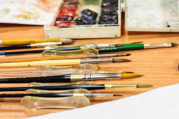 Paintbrushes and watercolors on wooden table background.