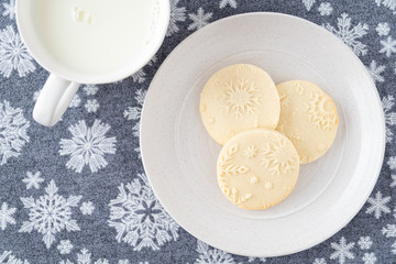 Homemade sugar cookies on a white stoneware plate, snowflake background, mug of milk