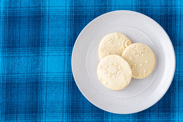 Homemade sugar cookies on a white stoneware plate, blue plaid background