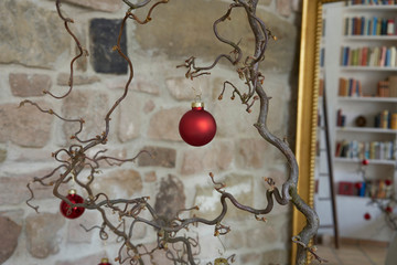 Detail of a red christmas tree ball at branch in front of stone wall in loft