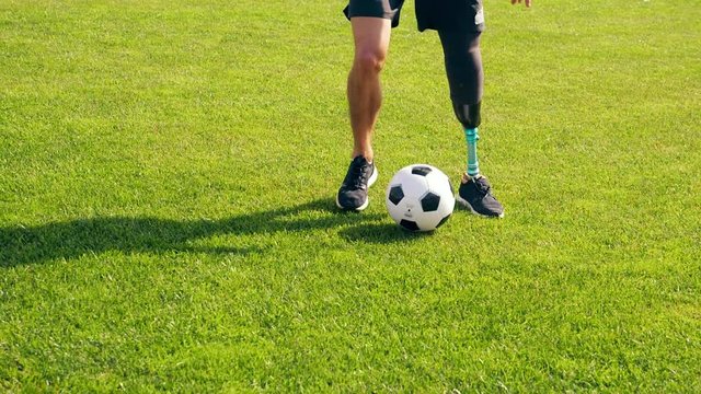 Green lawn with a ball getting kicked by a disabled man