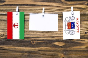 Hanging flags of Iran and Mayotte attached to rope with clothes pins with copy space on white note paper on wooden background.Diplomatic relations between countries.