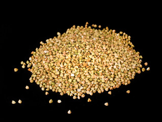 Heap of green buckwheat groats on black background. Top view.