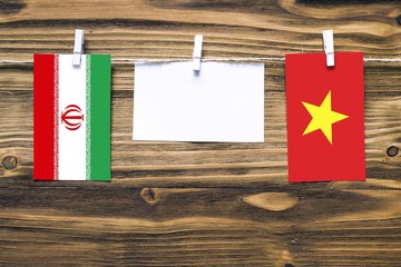 Hanging flags of Iran and Vietnam attached to rope with clothes pins with copy space on white note paper on wooden background.Diplomatic relations between countries.