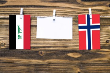 Hanging flags of Iraq and Norway attached to rope with clothes pins with copy space on white note paper on wooden background.Diplomatic relations between countries.