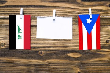 Hanging flags of Iraq and Puerto Rico attached to rope with clothes pins with copy space on white note paper on wooden background.Diplomatic relations between countries.