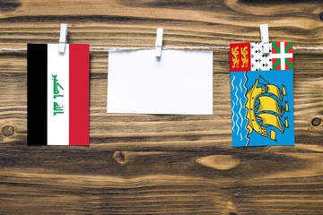 Hanging flags of Iraq and Saint Pierre And Miquelon attached to rope with clothes pins with copy space on white note paper on wooden background.Diplomatic relations between countries.