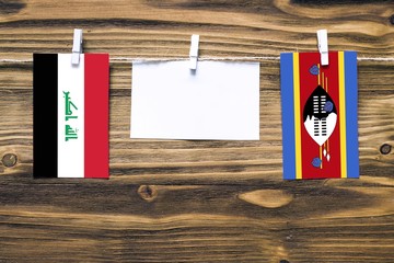 Hanging flags of Iraq and Swaziland attached to rope with clothes pins with copy space on white note paper on wooden background.Diplomatic relations between countries.