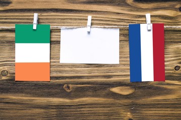 Hanging flags of Ireland and Netherlands attached to rope with clothes pins with copy space on white note paper on wooden background.Diplomatic relations between countries.