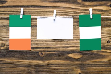 Hanging flags of Ireland and Nigeria attached to rope with clothes pins with copy space on white note paper on wooden background.Diplomatic relations between countries.