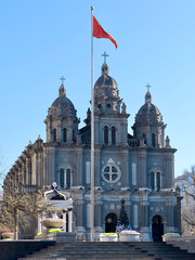 Fototapeta na wymiar Romanesque Revival style in architecture. St. Joseph's Church, Catholic church in Beijing. Red China flag in front of the facade. Christmas tree and decorations at the entrance to the church